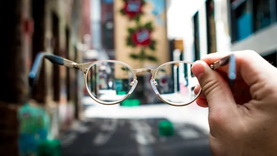A hand holding glasses in front of a city street