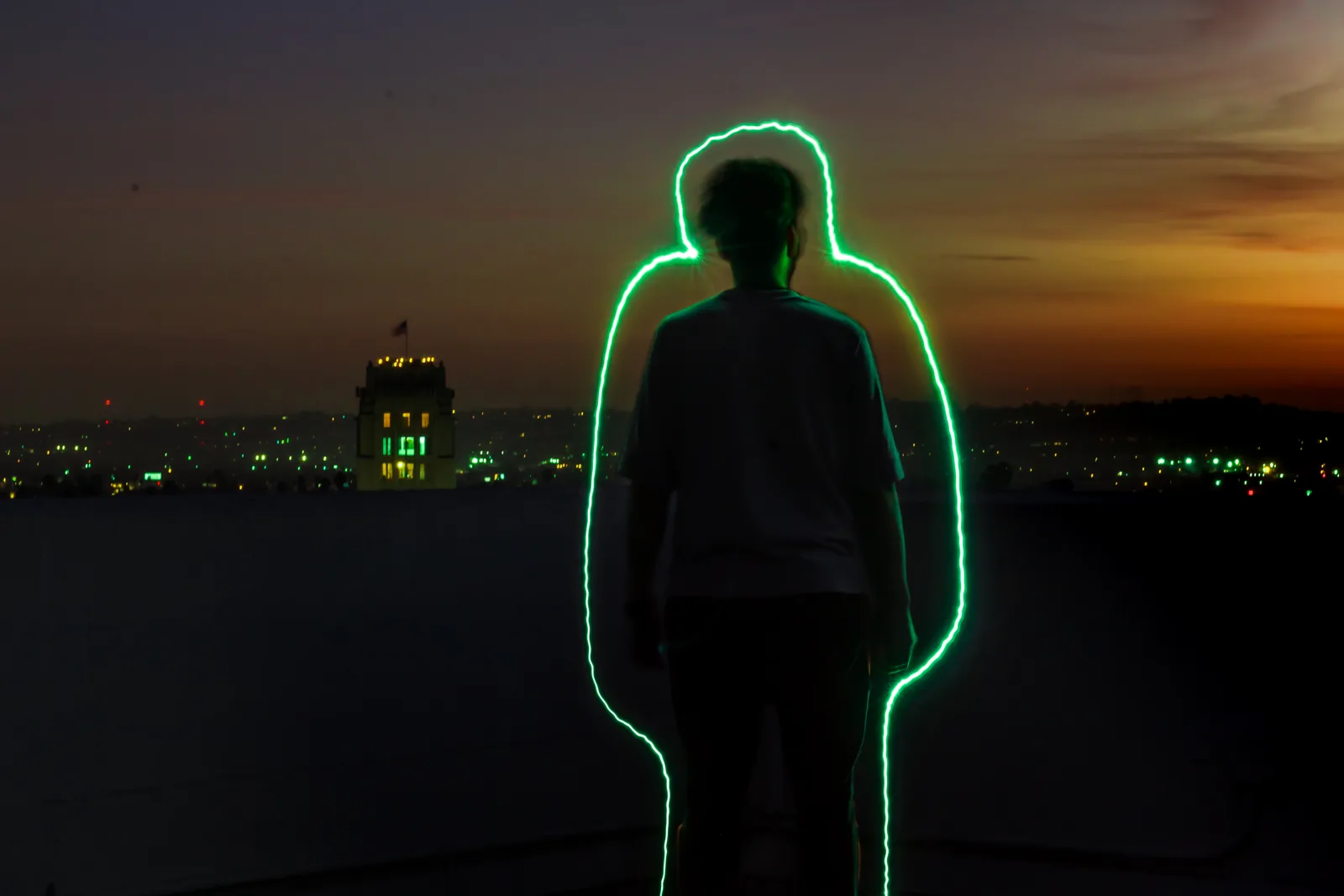 A person’s silhouette outlined in green against a city at dusk