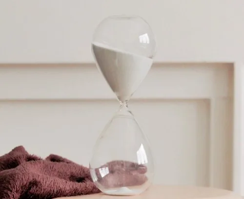 An hour-glass on a table with a red towel behind it.