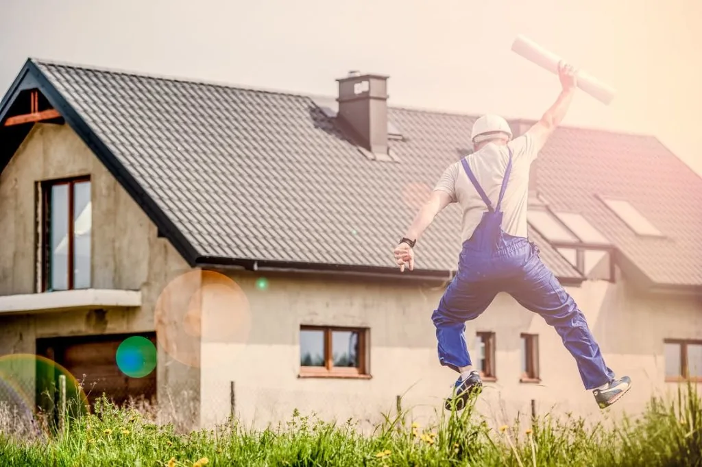 Man holding building plans and jumping outside house
