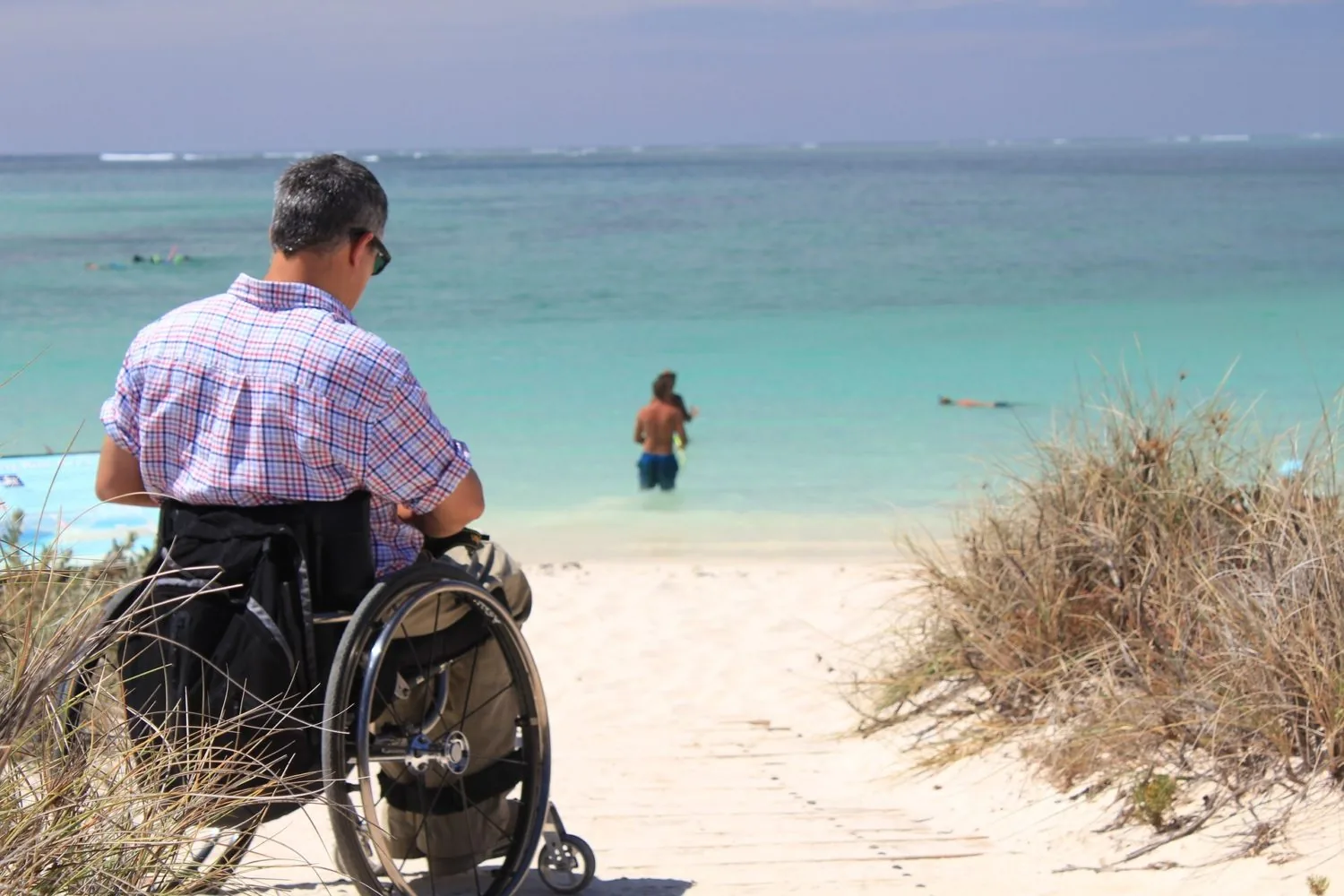 A wheelchair user beside a path leading to a beach