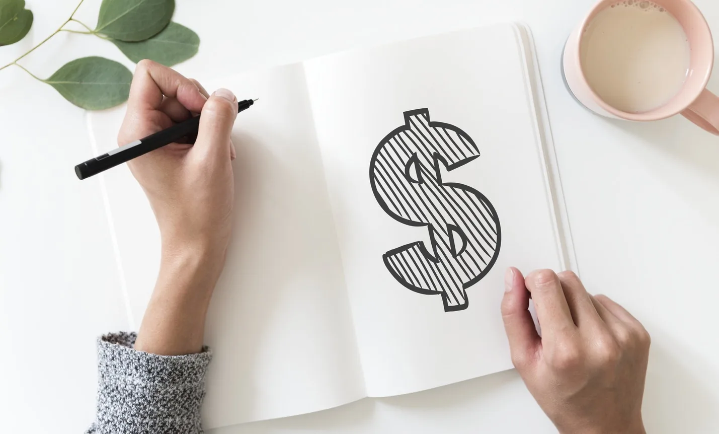 A person drawing a dollar sign in a notebook
