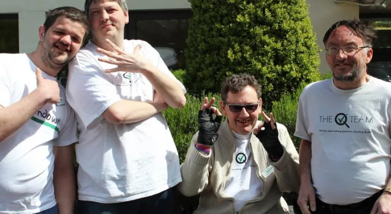 Four people posing together outdoors in the original Q-Team account