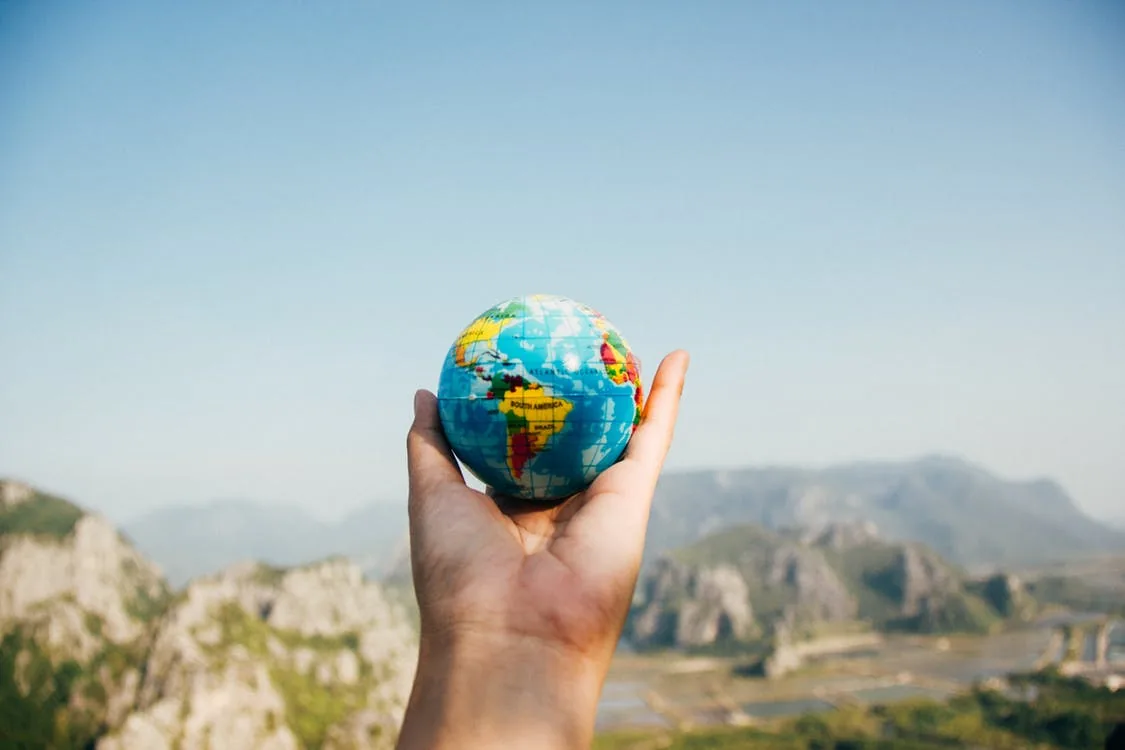 A hand holding a small globe in front of a landscape