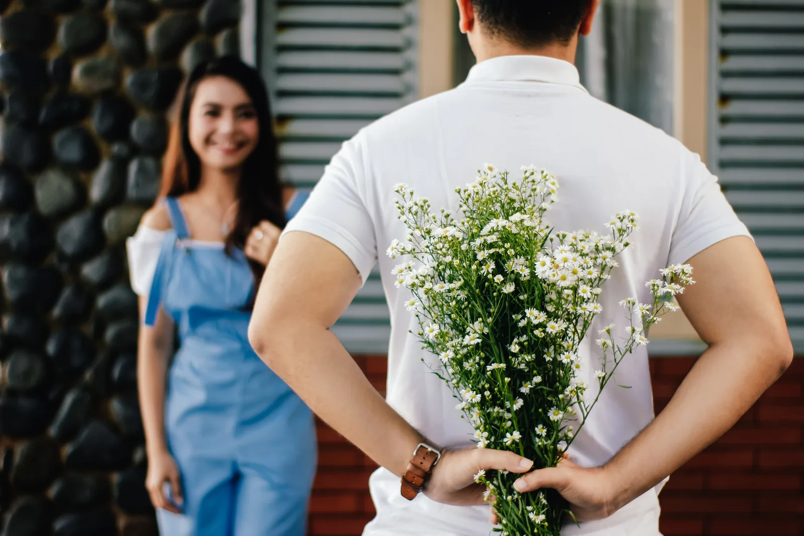 A person holding flowers behind their back while approaching another person