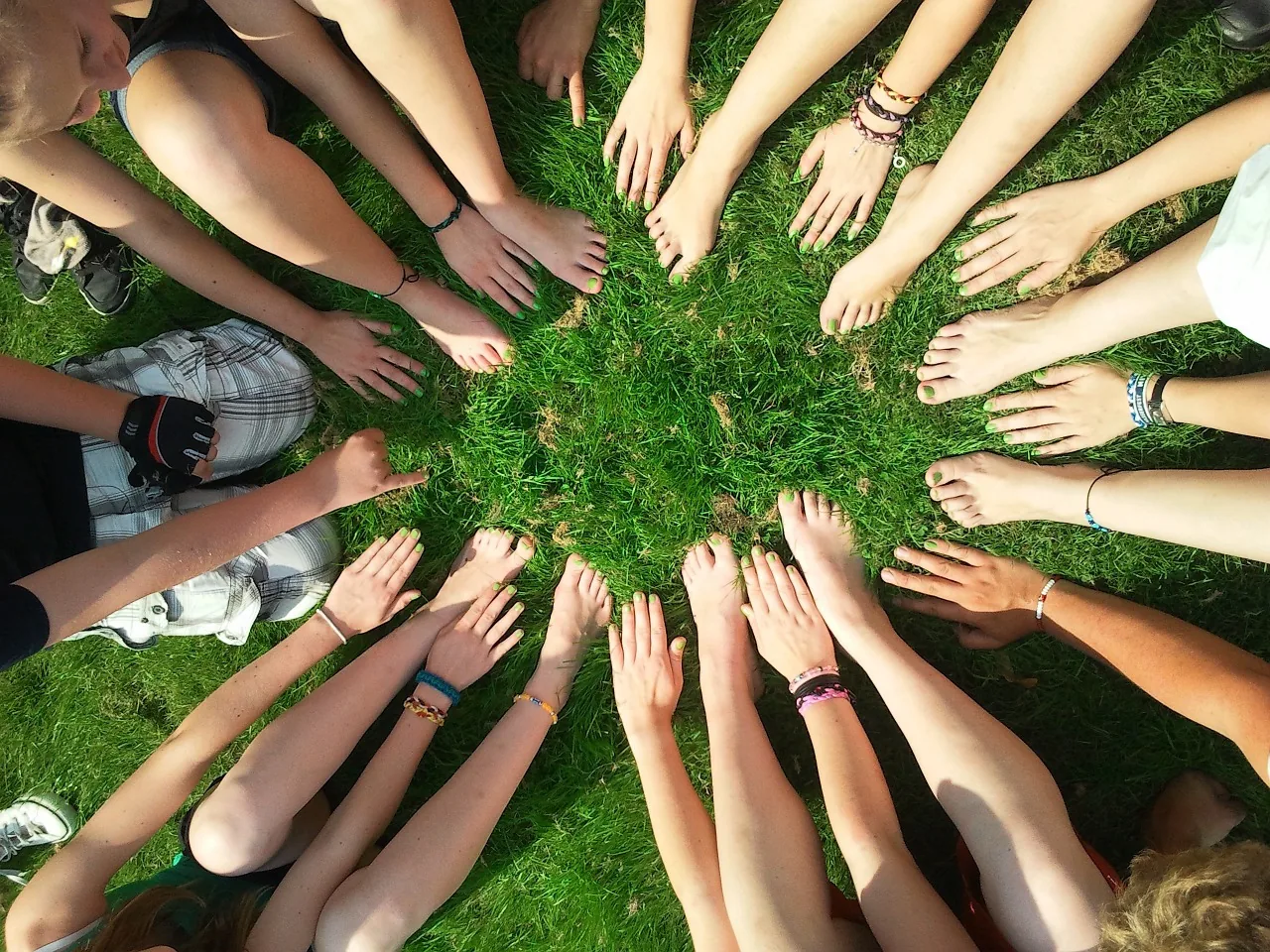 A circle of people reaching their hands towards the centre on grass