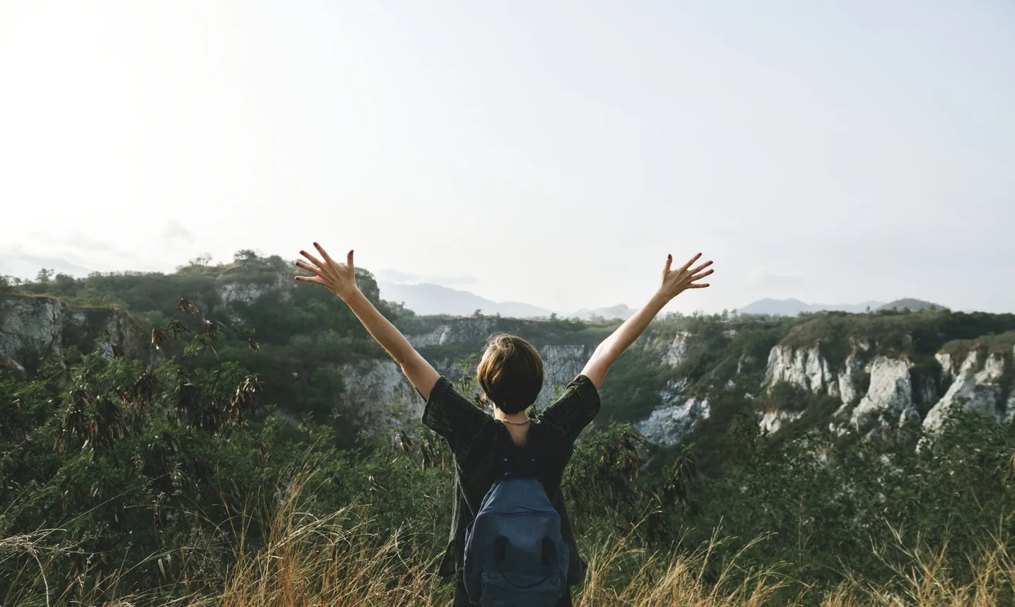 A person with raised arms looking over a landscape