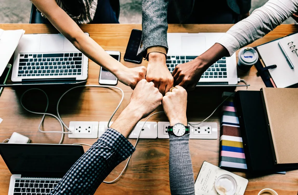 People stacking their hands above an office table with laptops