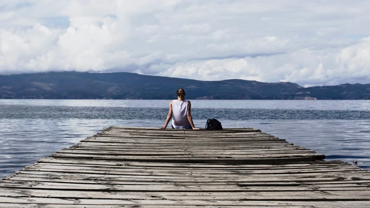 A woman sitting on the dock of a lake.