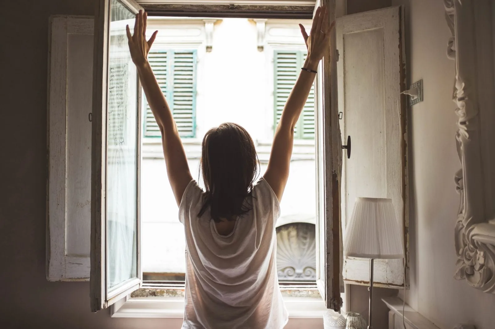 A person stretching their arms beside an open window