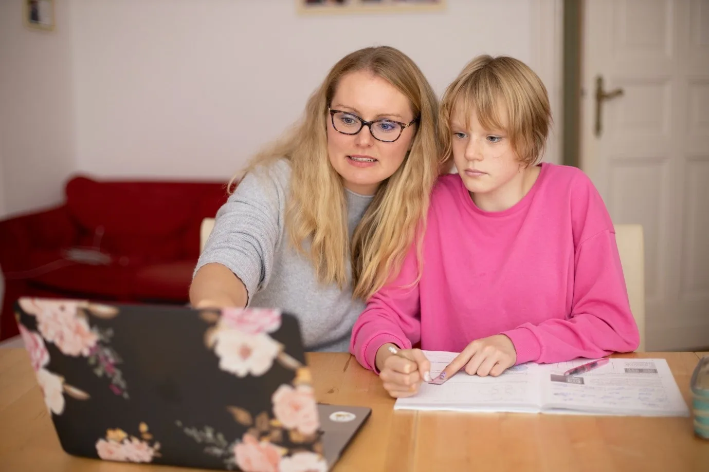 An adult wearing glasses seated beside a child using a laptop