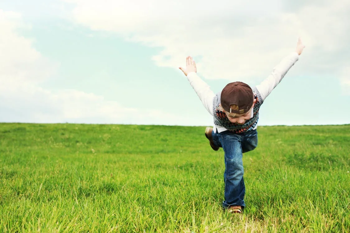 A child with arms raised in a grassy field