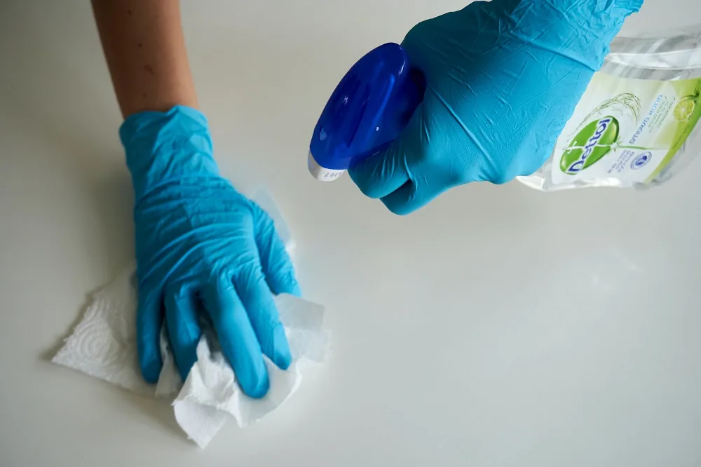 Gloved hands wiping a surface with a cloth and spray