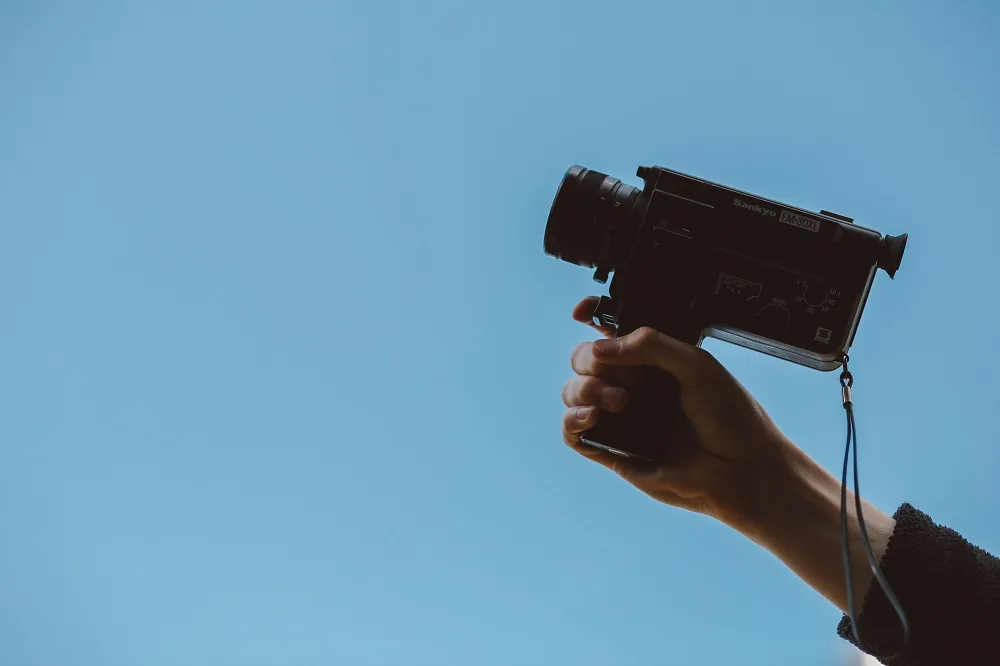 A hand holding a camera against a blue sky
